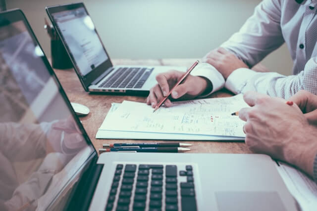 Two people take notes on a piece of paper beside their laptops.