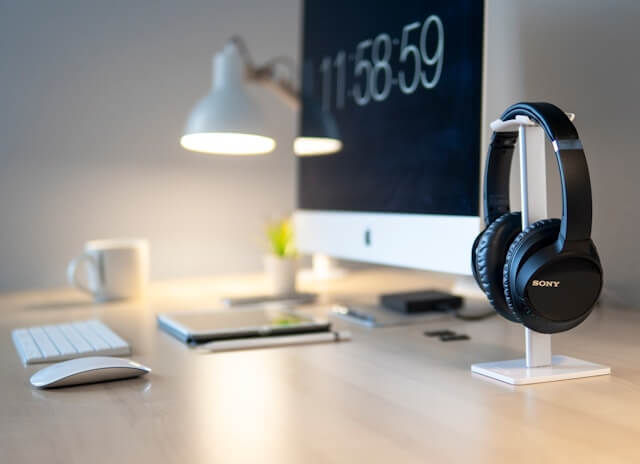 A clean desk has only a computer screen, a tablet, a pair of headphones and a lamp.