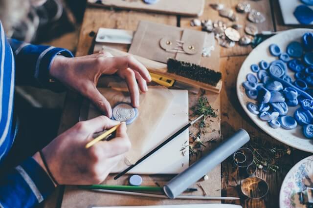 Top down view of a person working on something handmade with crafting supplies around them.