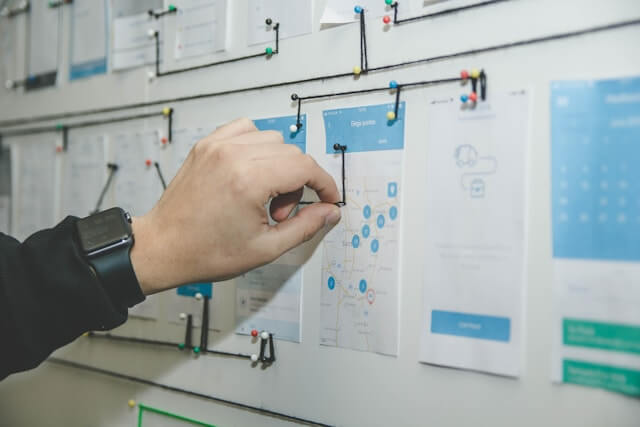 A hand pulling a string between some sticky notes and drawings hanging on a wall.