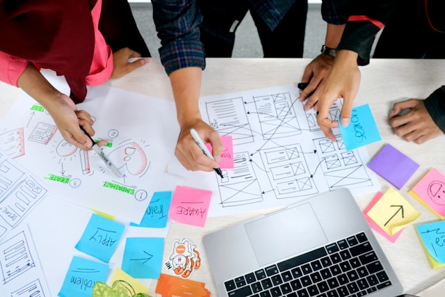 A group of people works together on UX design using sticky notes and quick sharpie drawings of web pages.