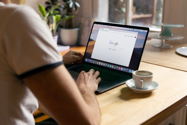 A person using google on their laptop with a mug of coffee next to them.