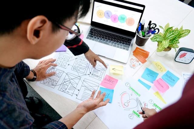A group of people looks down on some sketches and sticky notes of a website drawn out on paper.